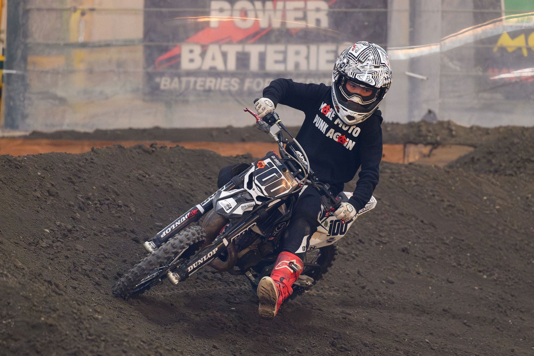 Motocross rider in action on a dirt track with sponsor banners in the background