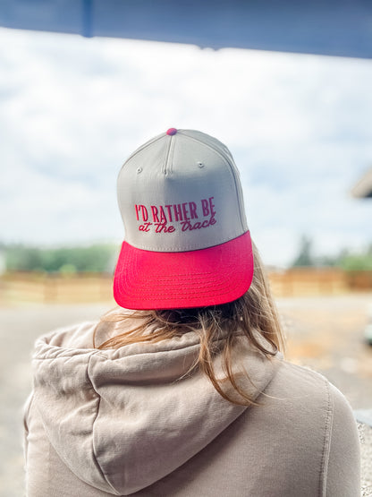 Person wearing a cap with 'I'd Rather Be at the Track' text, blurred background